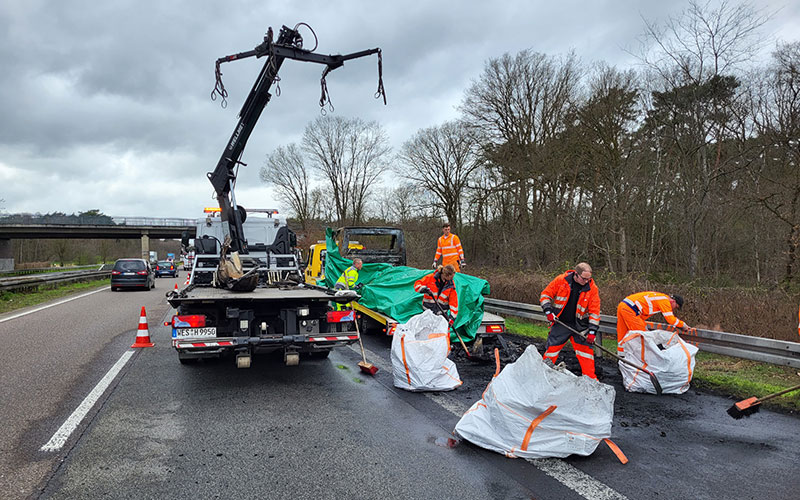 amf-abschleppdienst-unfallstellensanierung-4 Arbeiter räumen den Seitenstreifen einer Autobahn nach einem Unfall auf. Ein Bergunsfahrzeug mit Kran steht auf dem rechten Fahrstreifen.